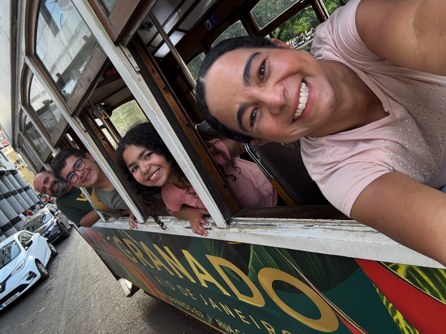 Janderson, Patricia and their two children leaning out of the window of an old tram, all smiling.